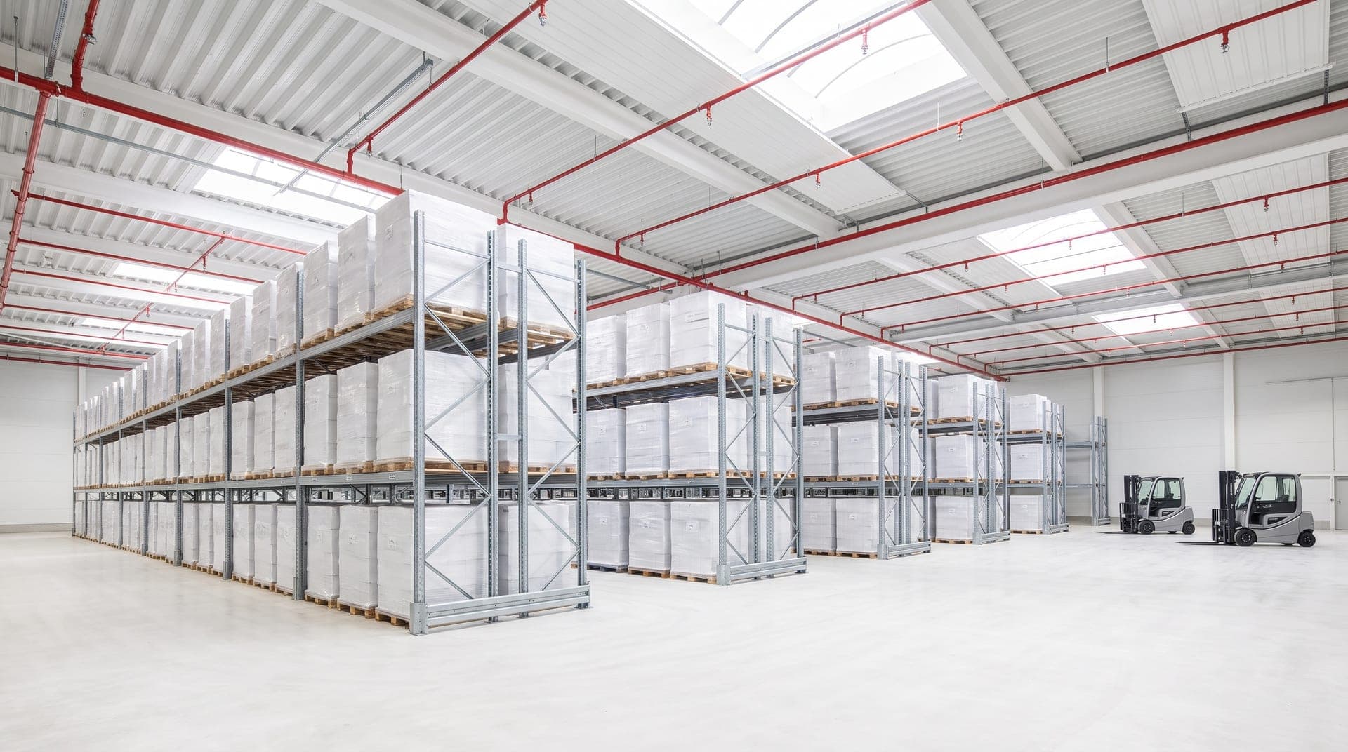 Réseau sprinkler neuf peint en rouge sous la toiture d'un entrepôt logistique rangé, têtes alignées au-dessus des allées de racks